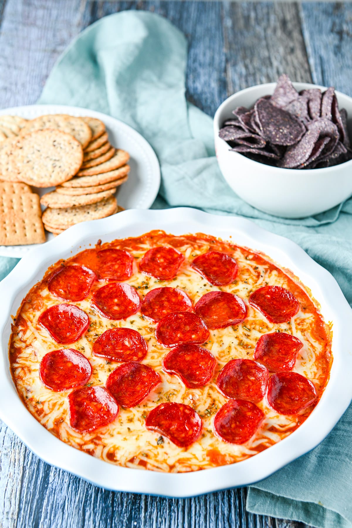 Chips and crackers in back of the pie plate with the cheesy dip with pepperoni