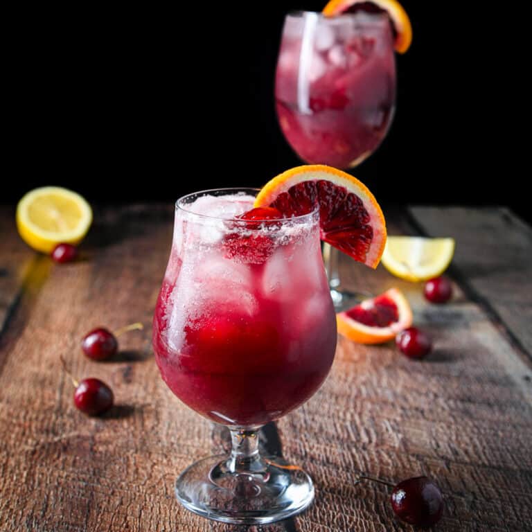 Square photo of two glasses with the wine drink it them with fruit slices on the rim and on the table