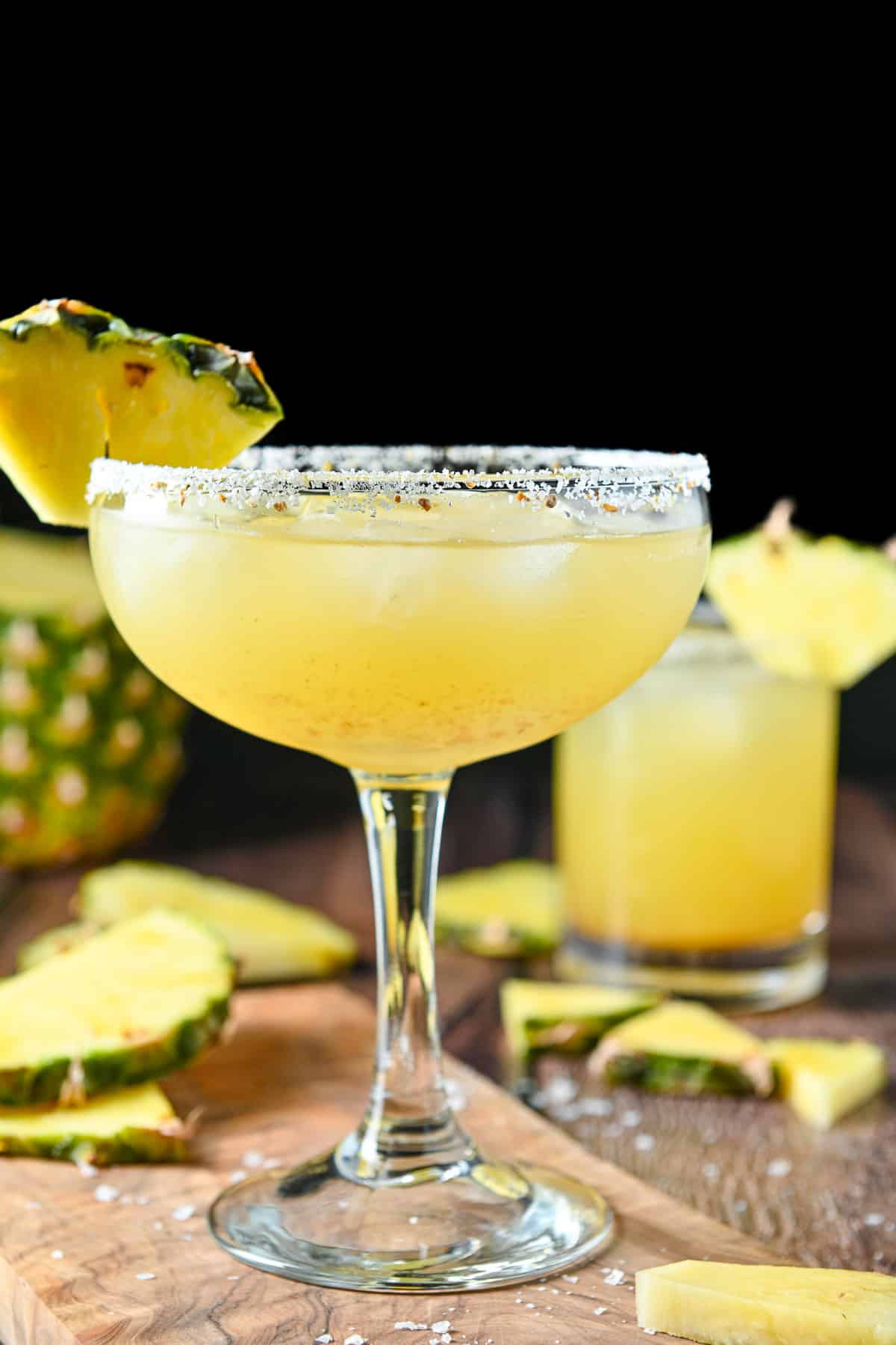 Vertical view of a bowl type margarita glass with salt and a wedge of pineapple on the rim