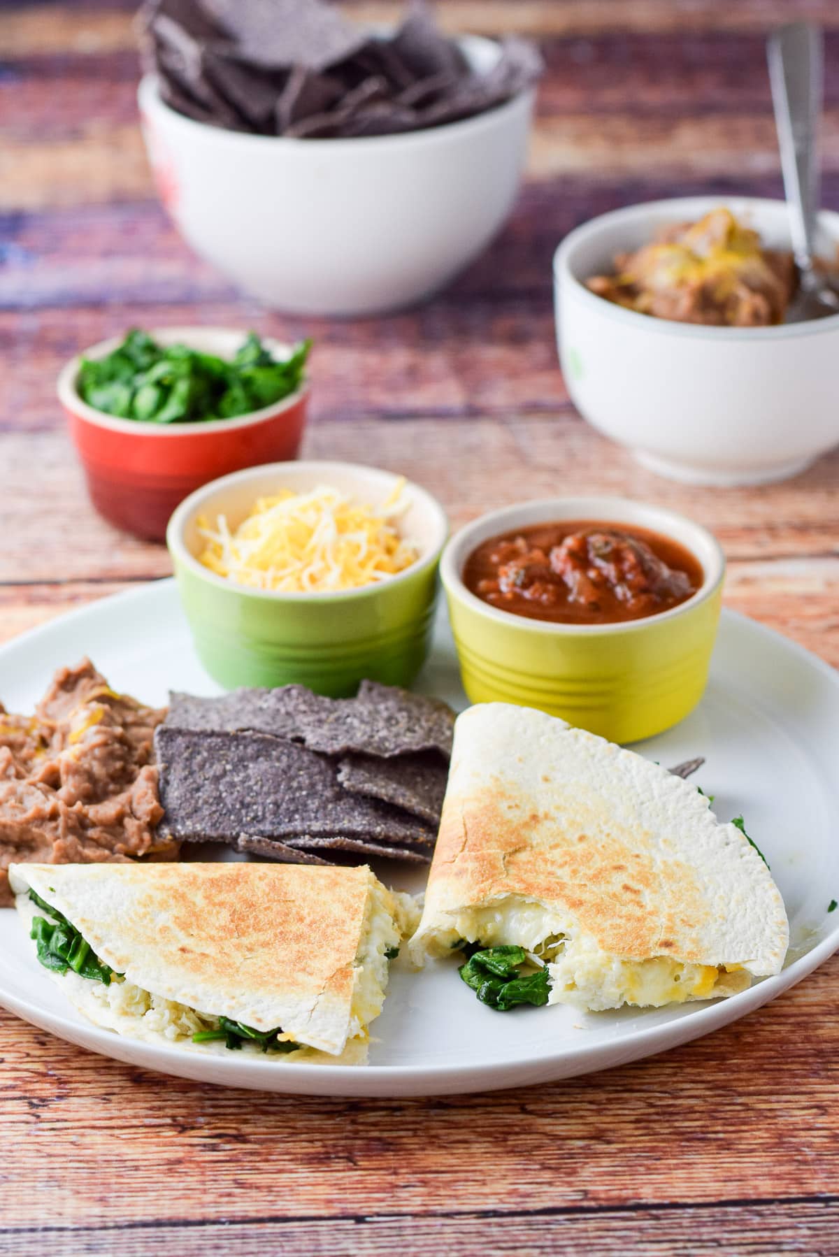 Two halves of the quesadilla with salsa, cheese, spinach, beans, and chips in the back