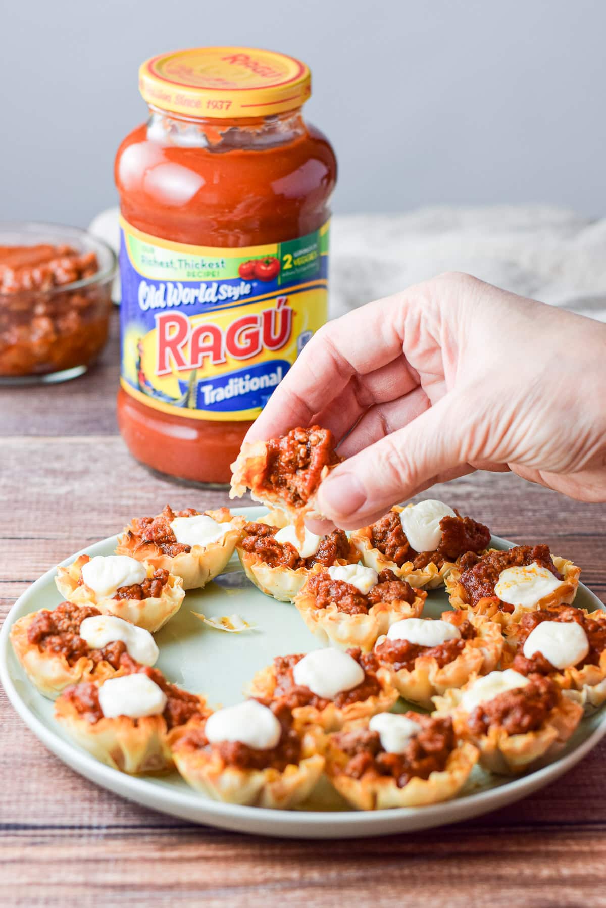 The woman's hand holding the appetizer with a bite out of it over the platter with the sauce in the back