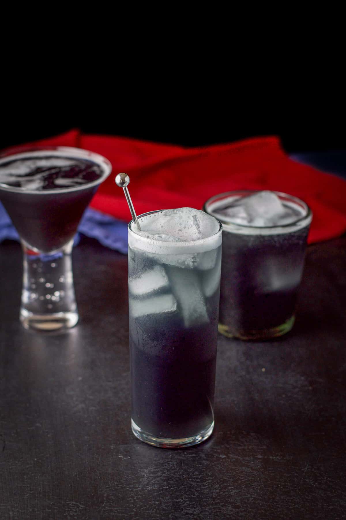 Three glasses with the purple cocktail the tall one in front
