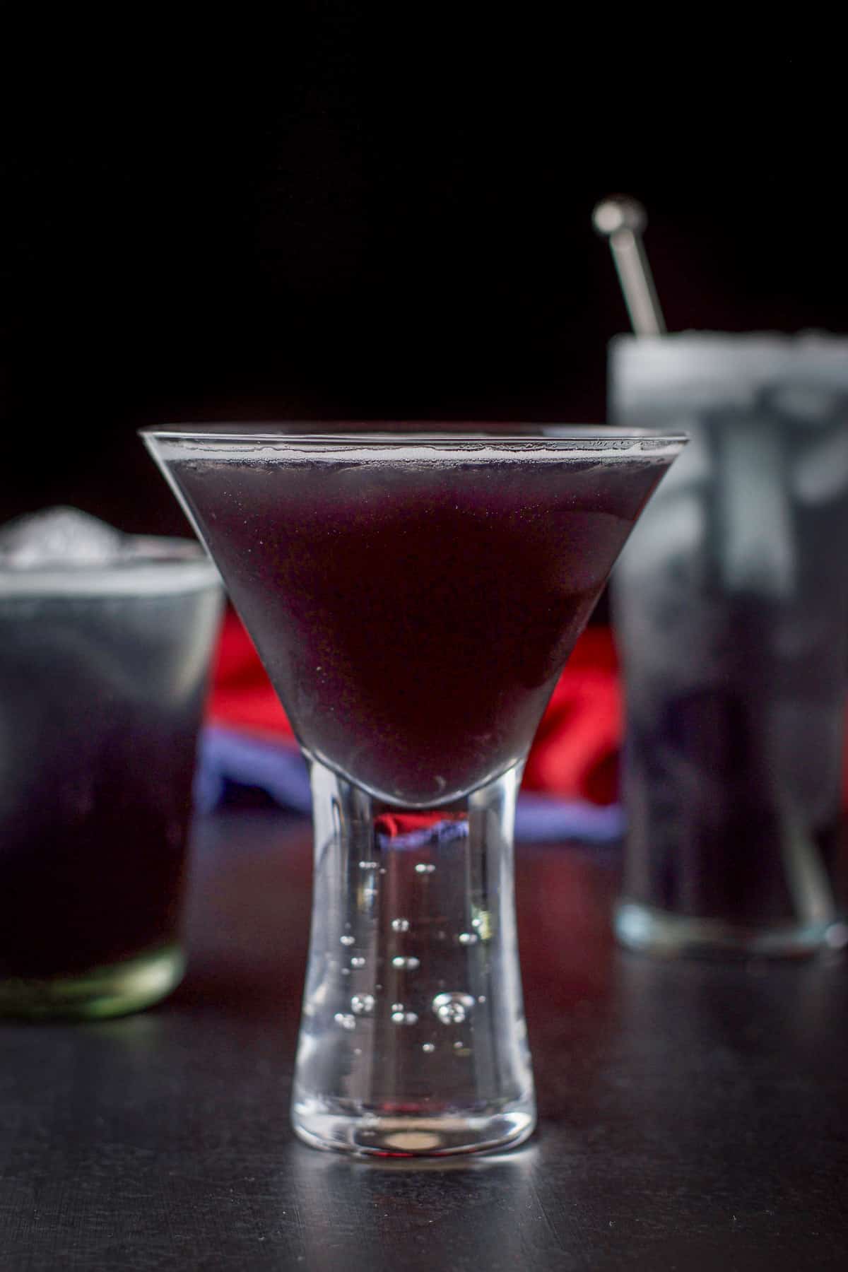 The bubble martini glass filled with the purple cocktail in front of the other two in vertical view