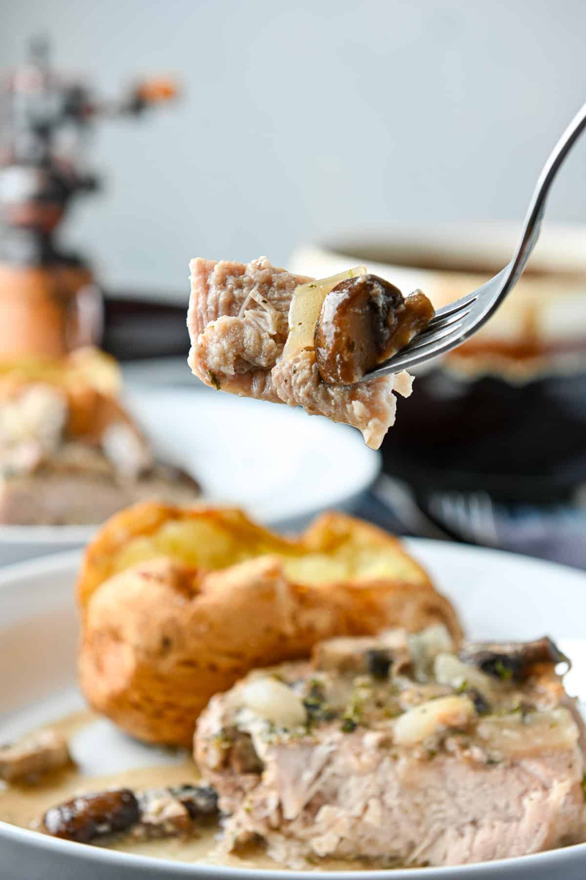 a fork with a piece of pork on it along with a mushroom and onion held over the plate of the meal