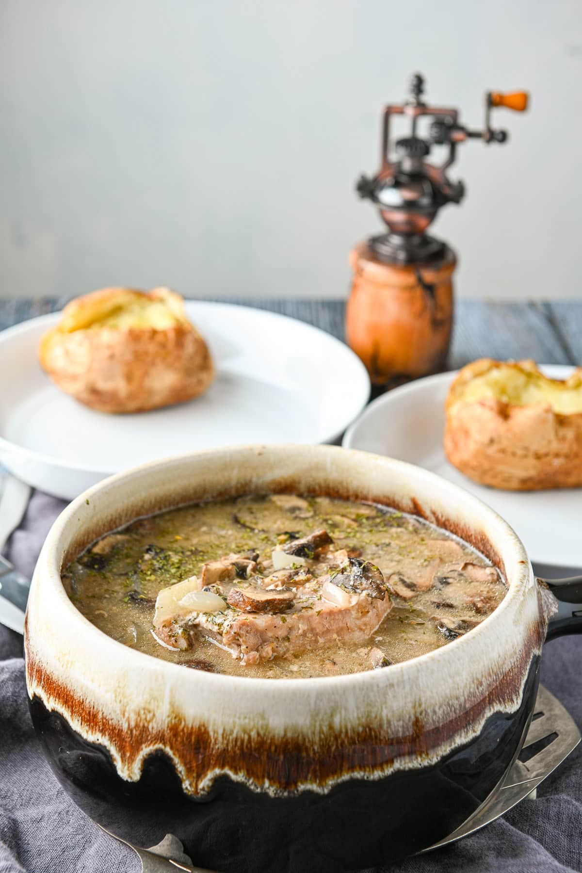 A big soup tureen filled with the pork chops and broth with two white plates with potatoes on them in the back