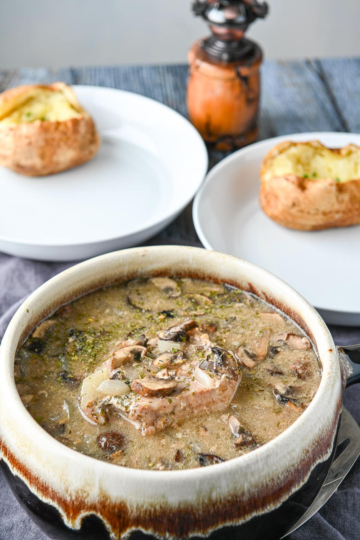 pork chops and broth in a big soup tureen with two white plates with baked potatoes on them in the back