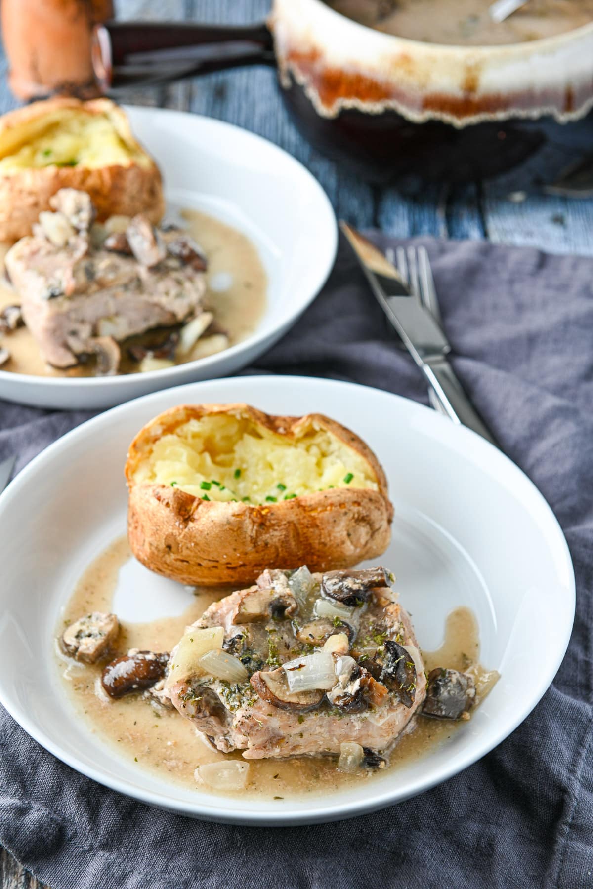 Two white plates with potatoes and pork with mushrooms and broth on them