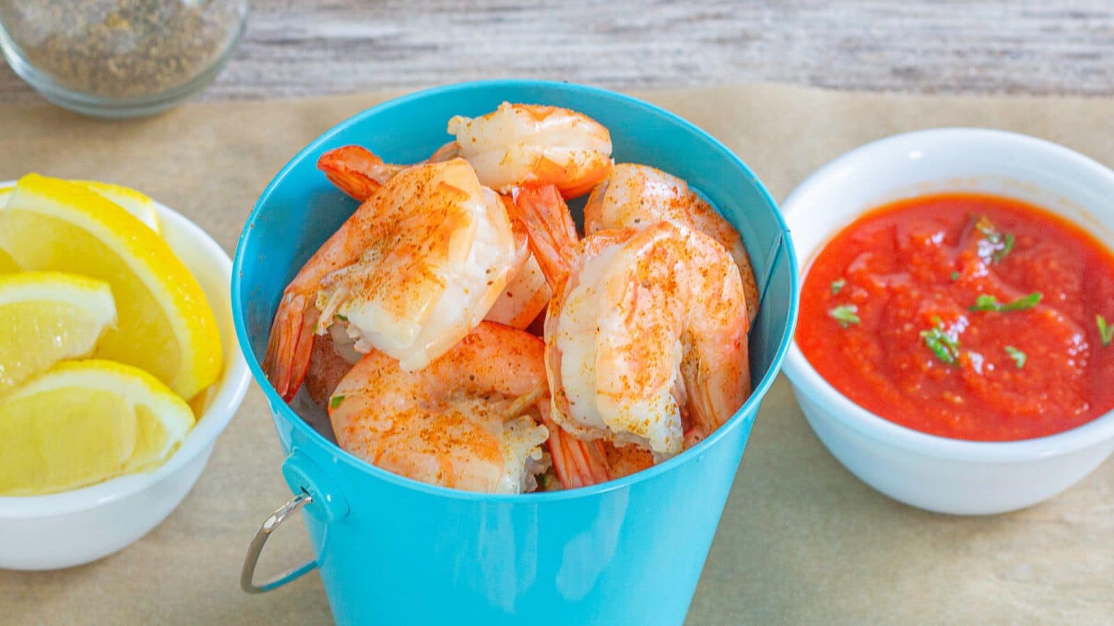 A blue pail with shrimp in it, on the side are lemon slices and cocktail sauce