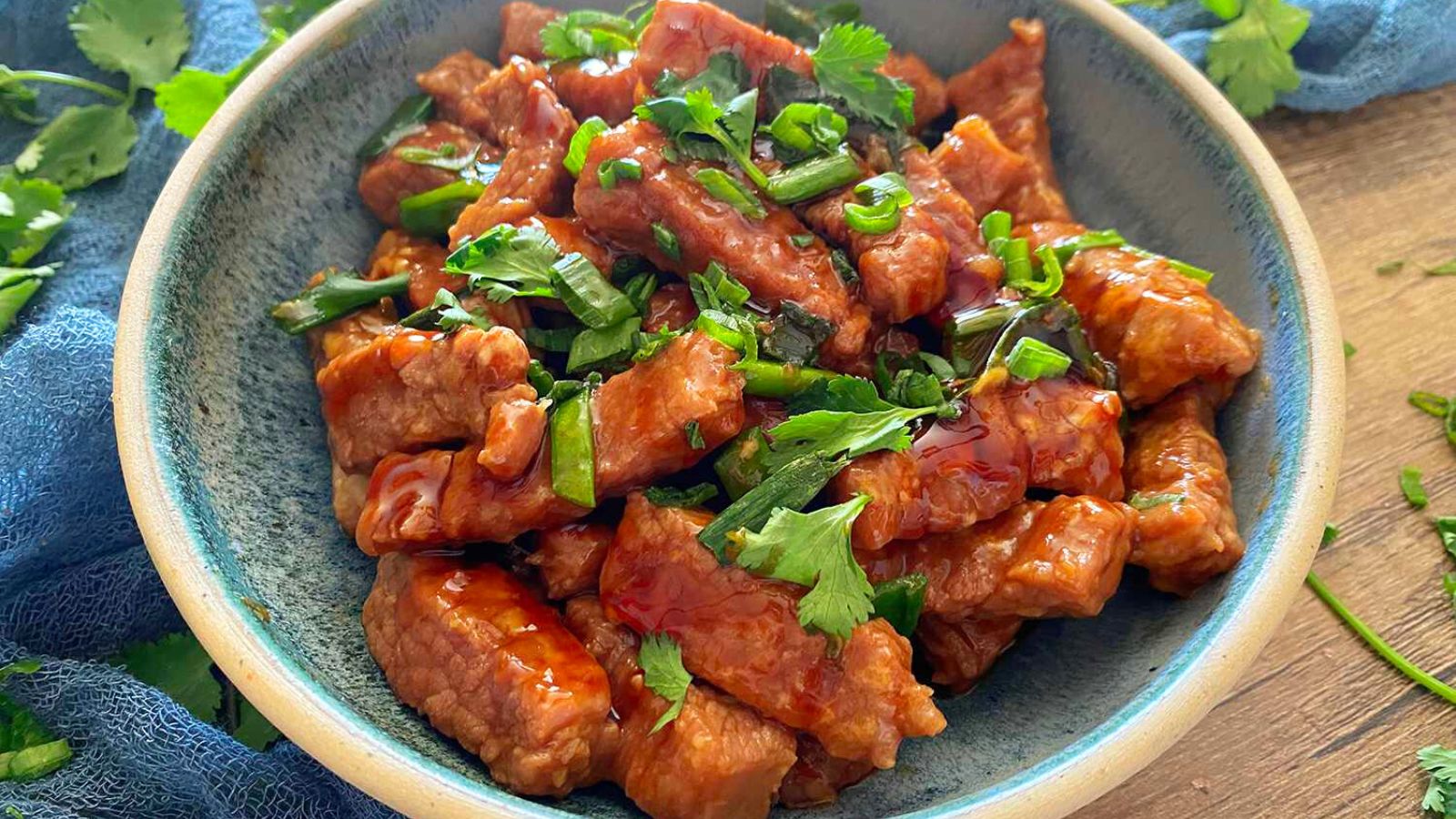 A blue-green plate with a saucy beef on it with parsley sprinkled on top