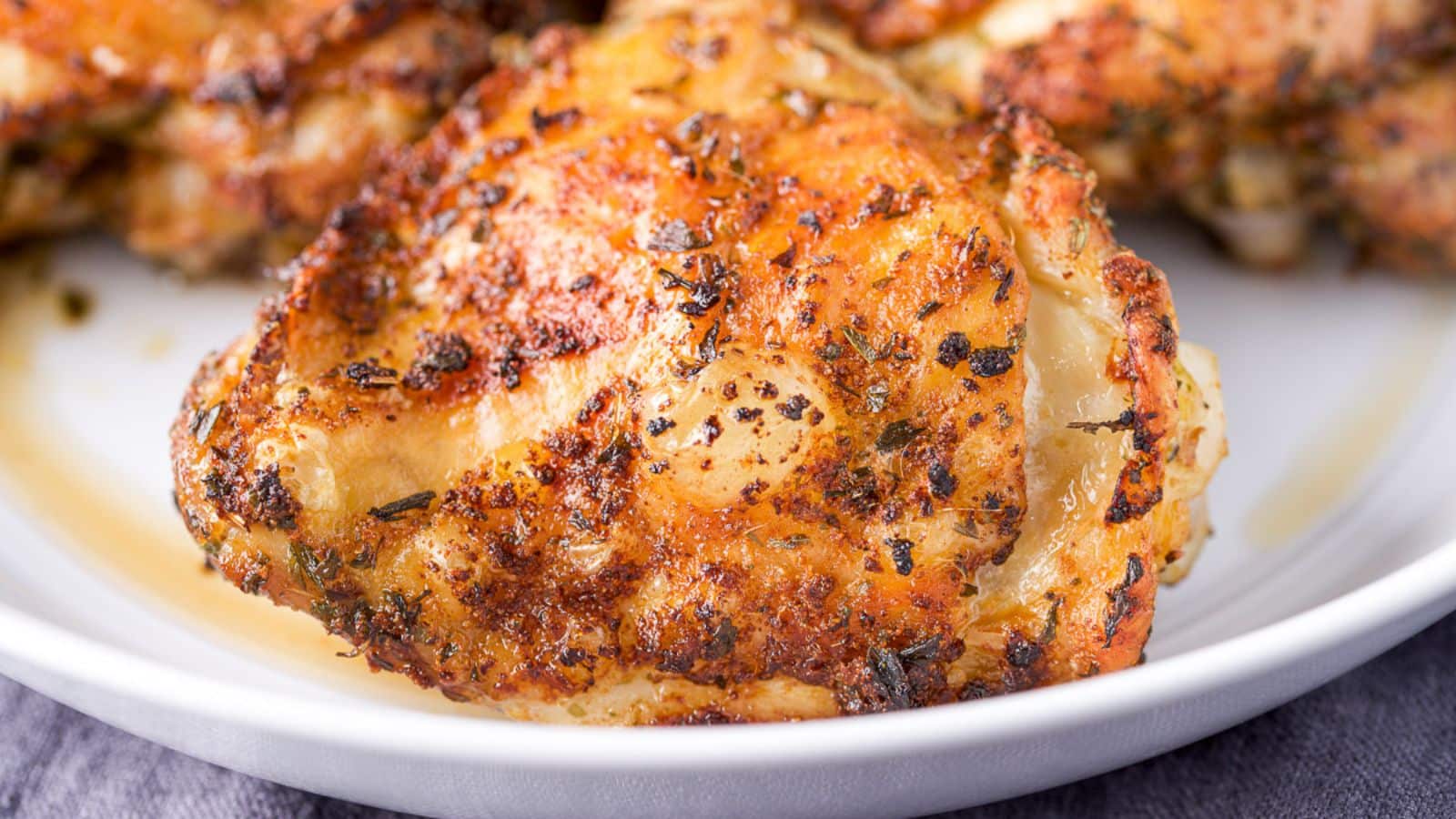 Close up of chicken thighs on a white plate with crispy skin