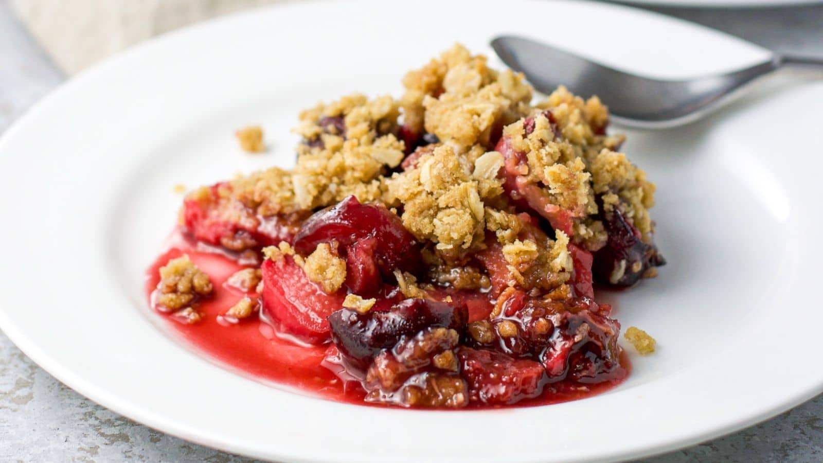 a white plate with a spoon on it along with a cherry crisp dessert