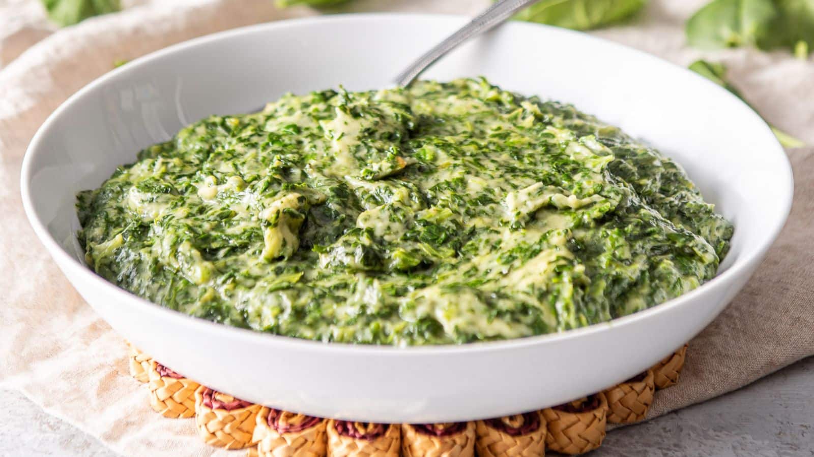 A white deep bowl filled with the spinach with cream