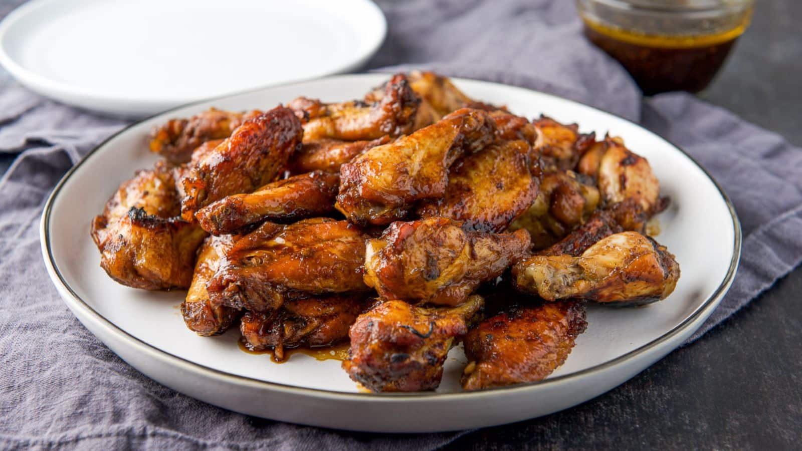 A plate with wings piled up on it with dipping sauce and another plate in back