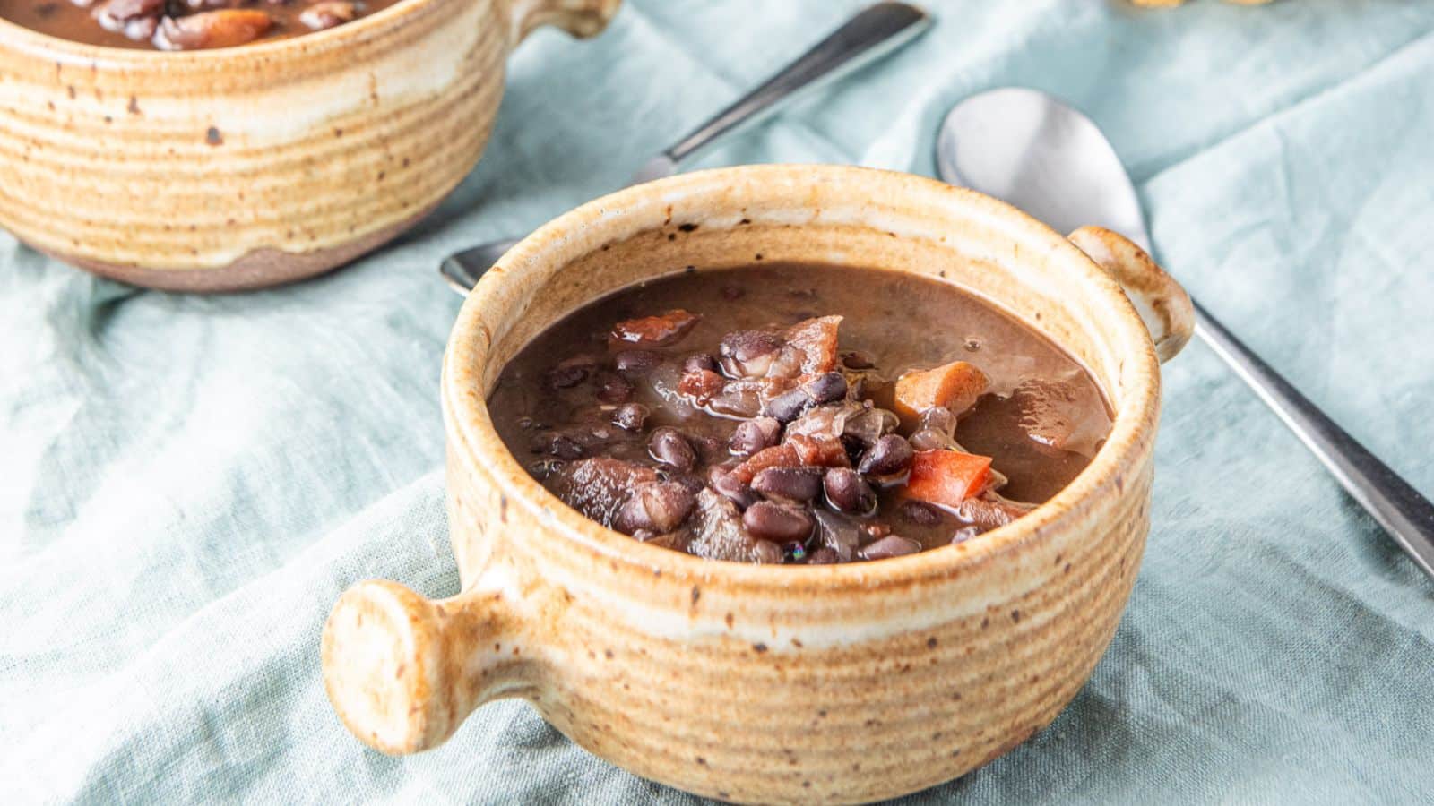 Black beans and carrots soup in a crock with two spoons on a green napkin