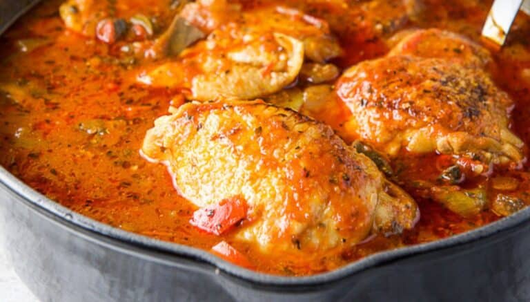 A pan with chicken and red gravy in it with vegetables and a ladle