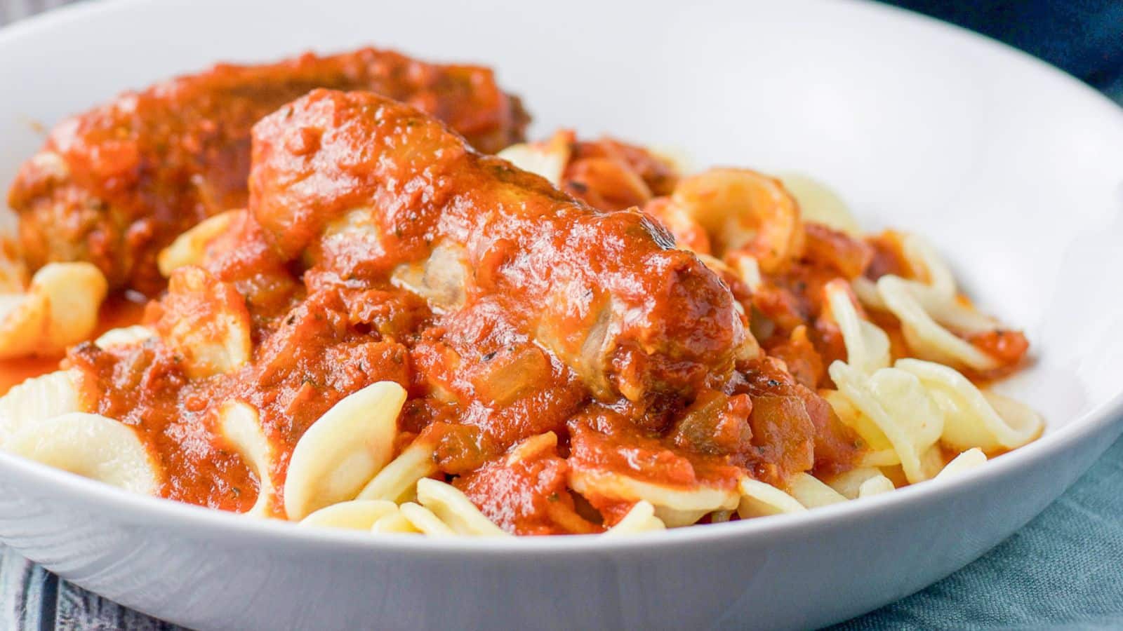 A white deep bowl with pasta, sauce and sausage