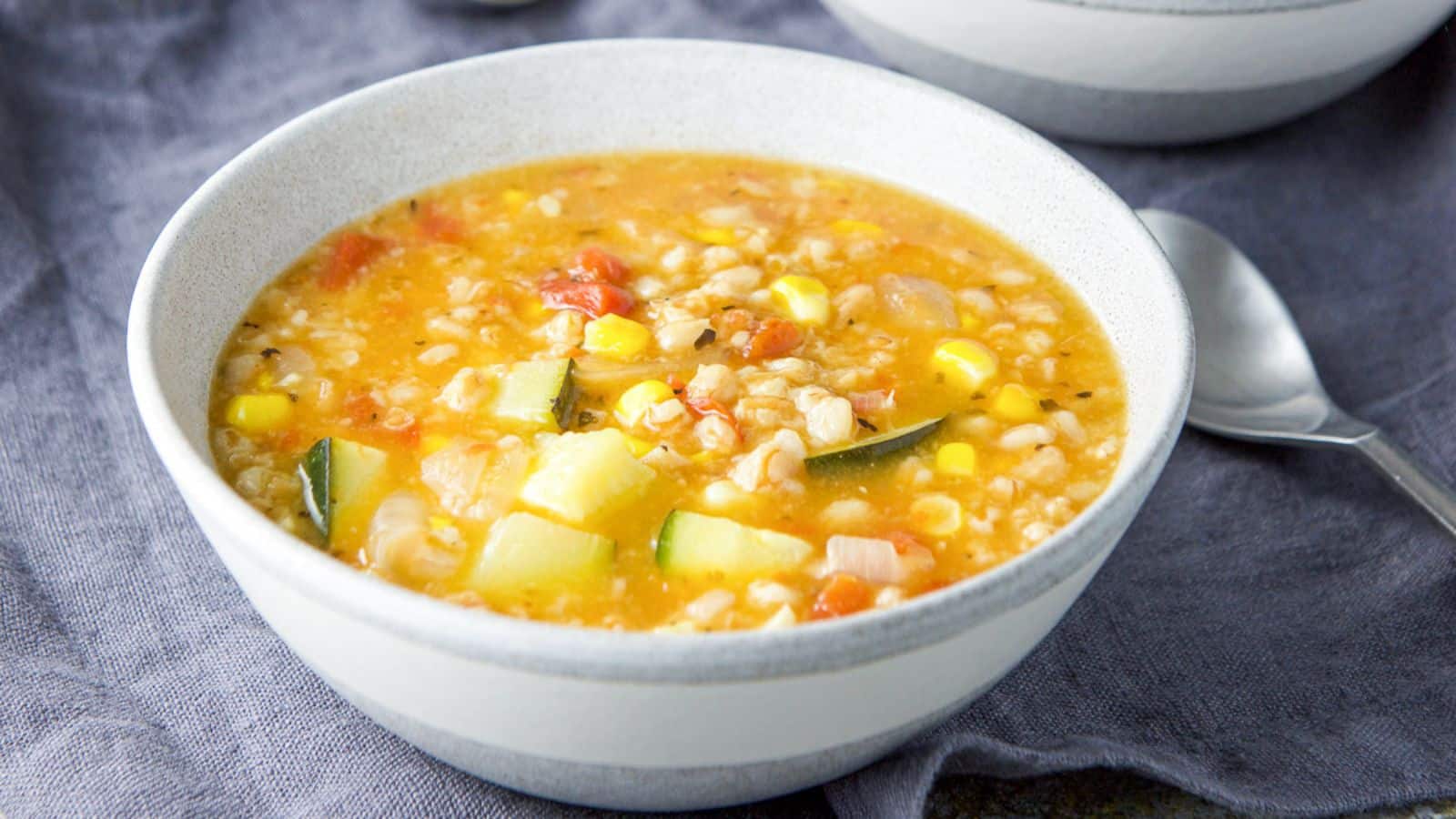 A grey bowl filled with a vegetable soup with a spoon and on a grey napkin