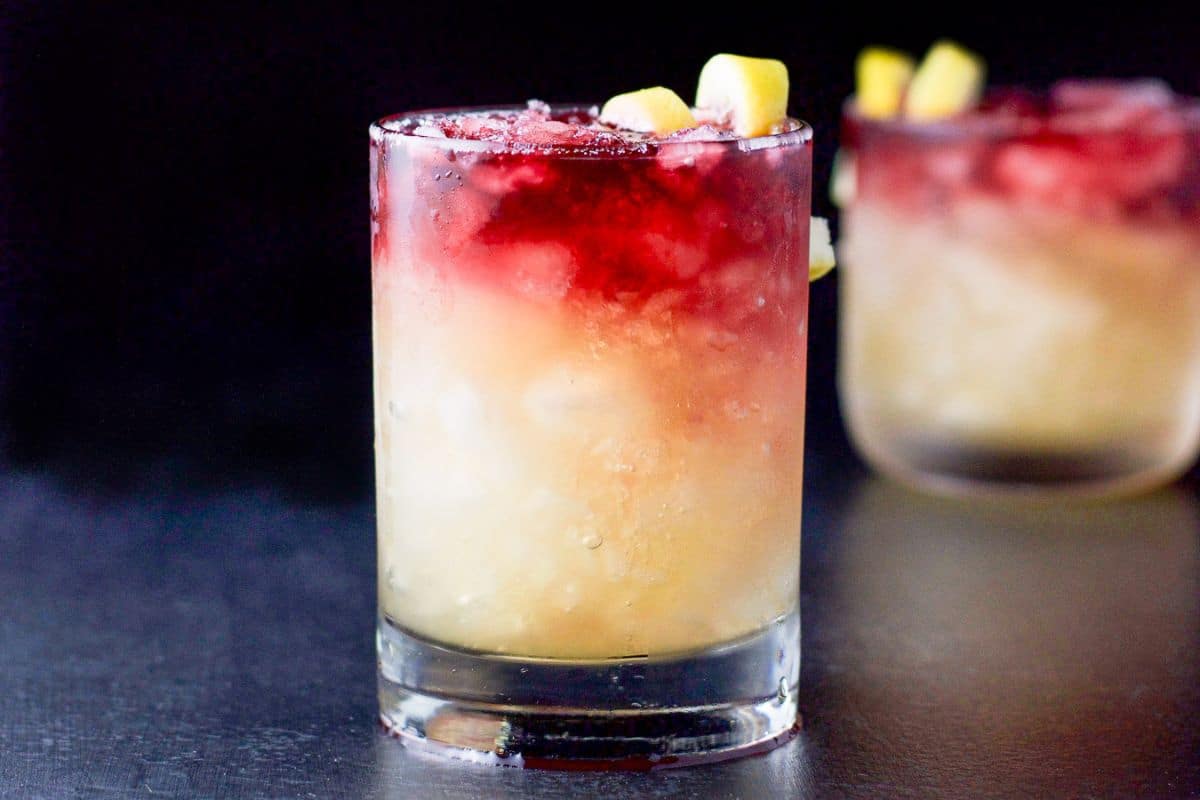 Two double old fashioned glasses filled with the sour drink with wine layered in the top