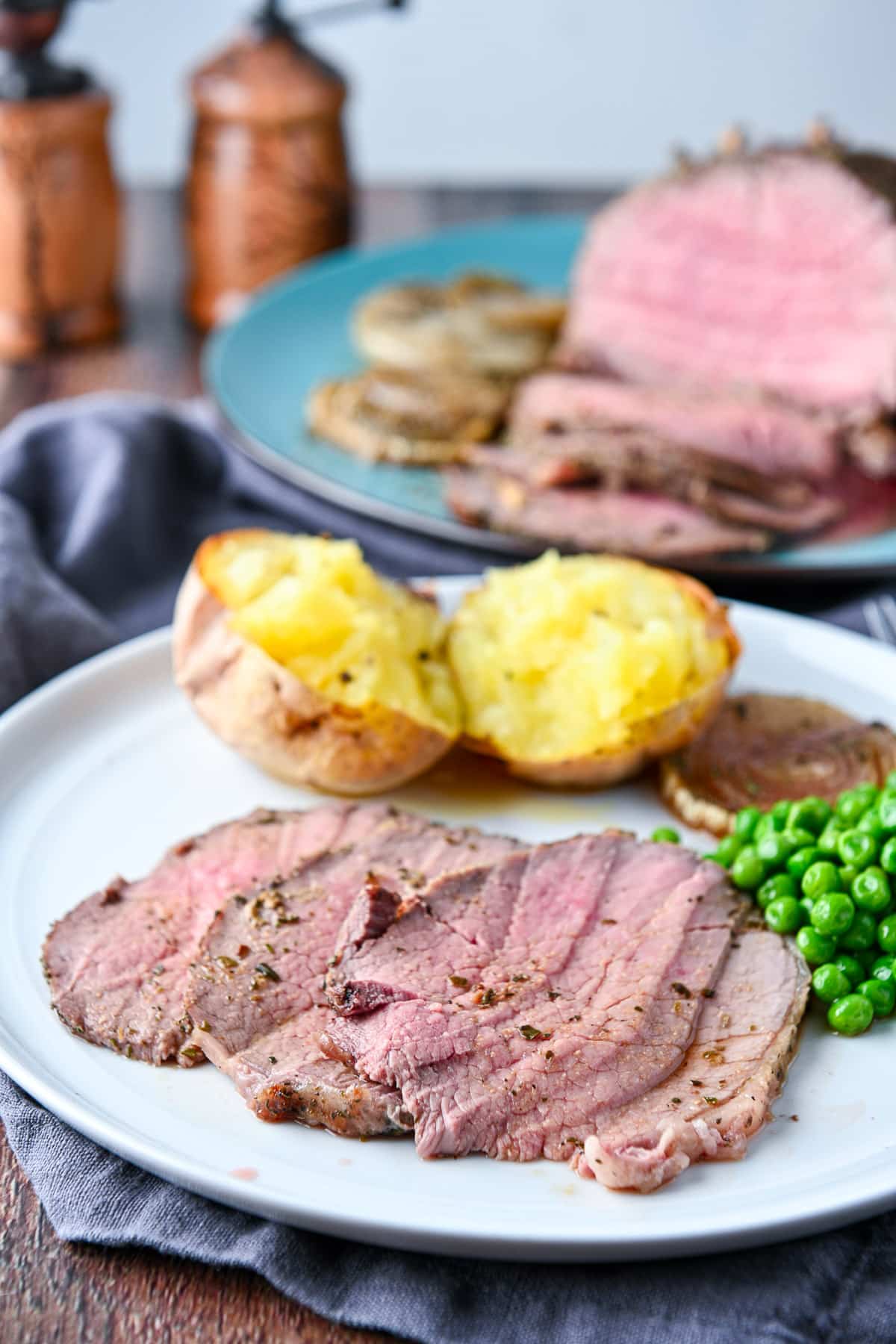 A plate with sliced beef on it with vegetables with the platter of meat in the back