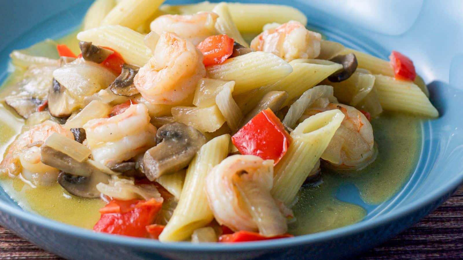 a deep blue plate with shrimp scampi in it with penne pasta and vegetables