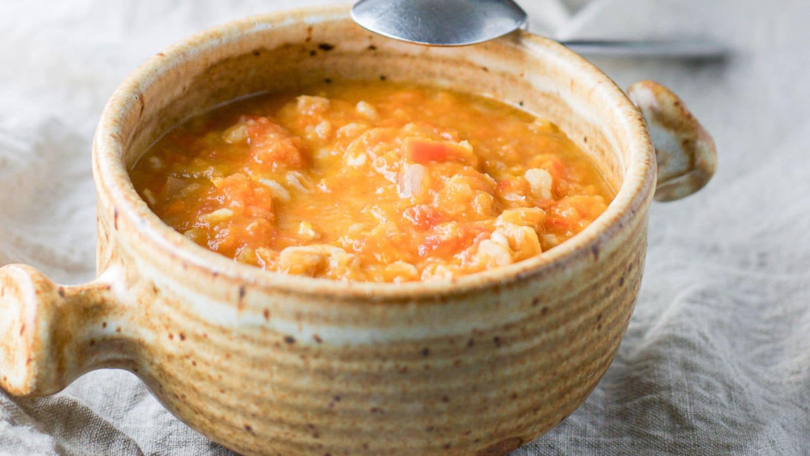 a brown bowl filled with the bean soup with a spoon on the side of the bowl