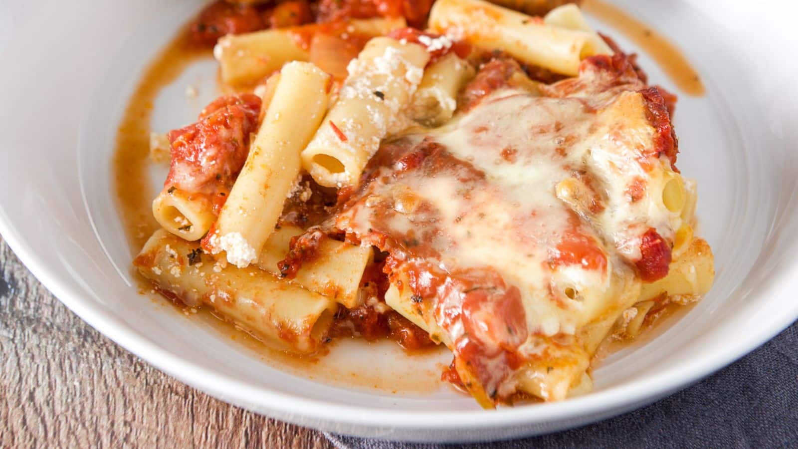 A white deep white plate filled with ziti, cheese, and a red sauce