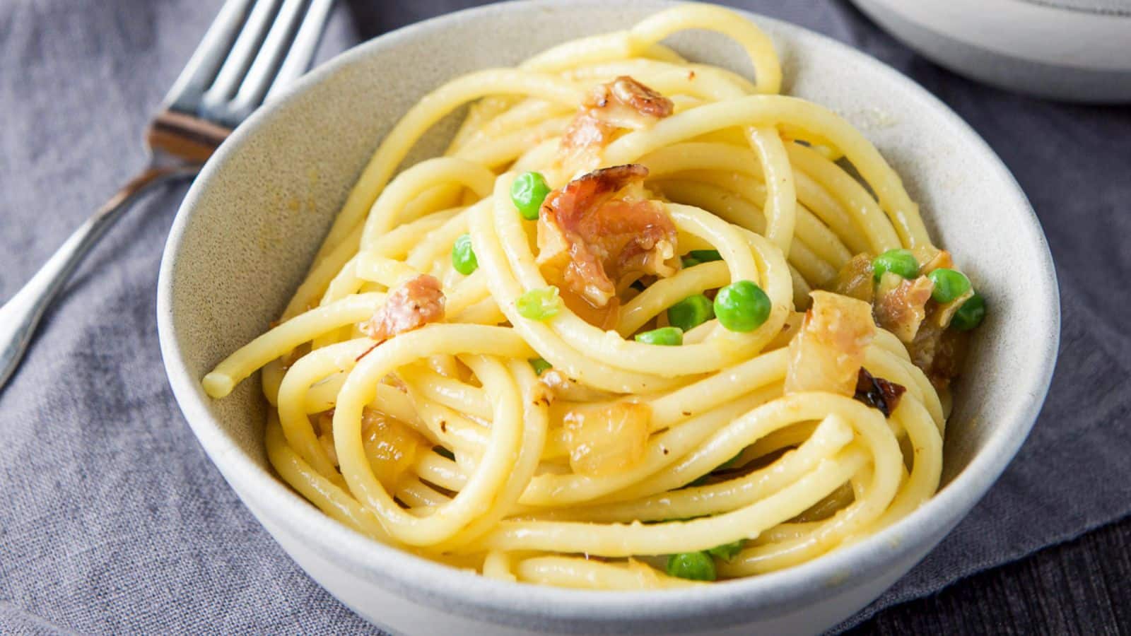 A grey bowl with bucatini with peas and pancetta