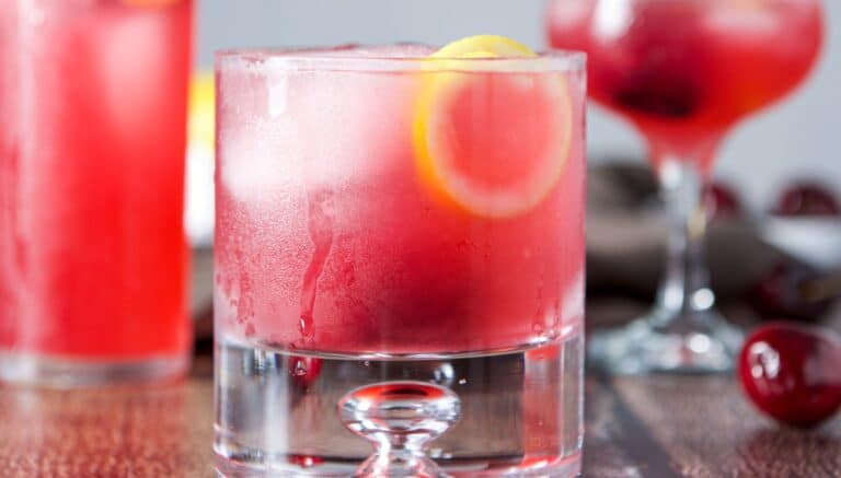 vertical view of the cherry drink with a lemon twist and cherry as garnish