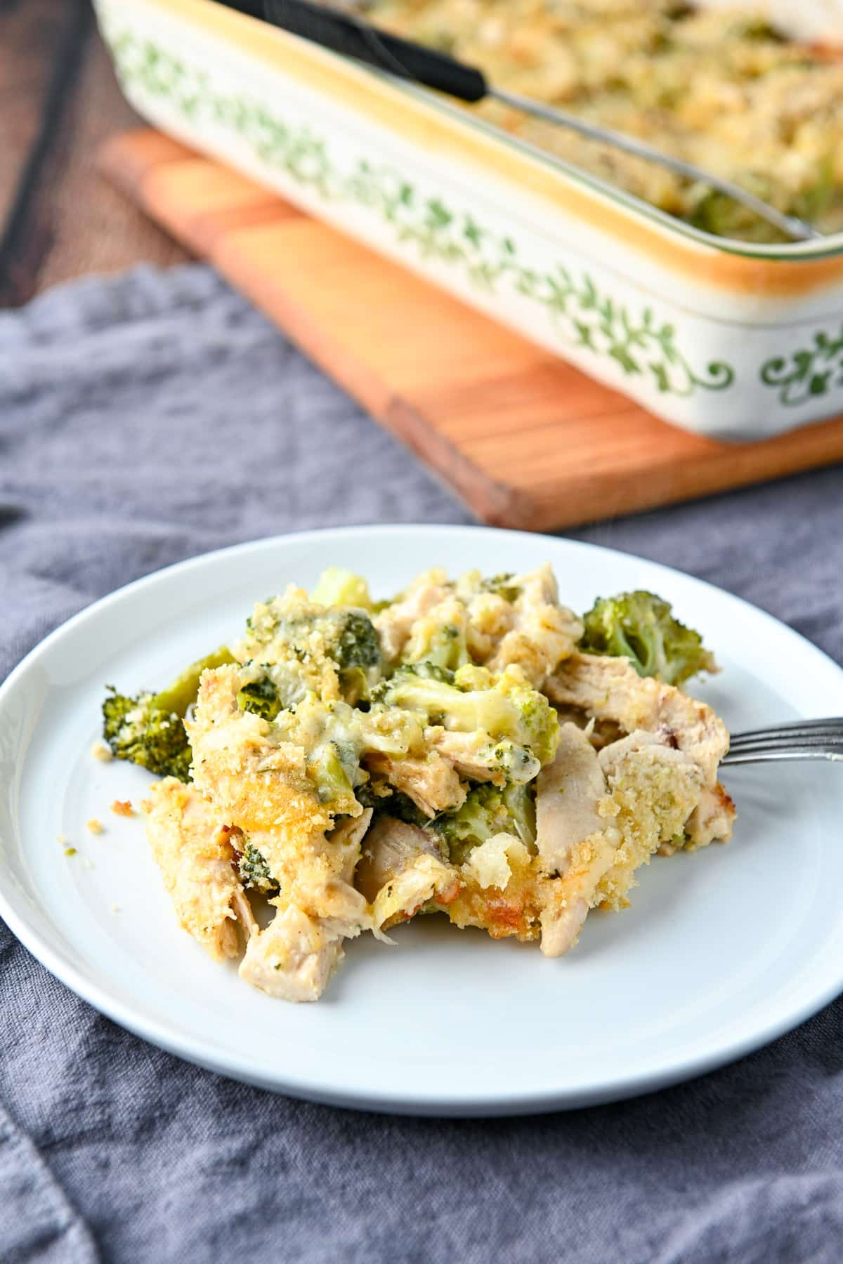 A small white plate with the spoonful of the chicken broccoli meal on it with the pan of it in the back