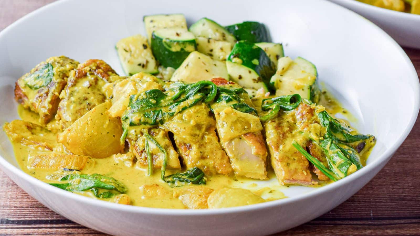 A white deep bowl with a breast of duck with curry sauce on it along with some zucchini