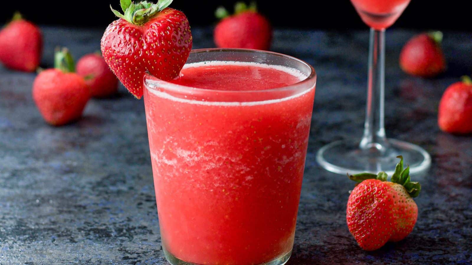 a double old fashioned glass with frozen red cocktail with strawberries as garnish and on the table
