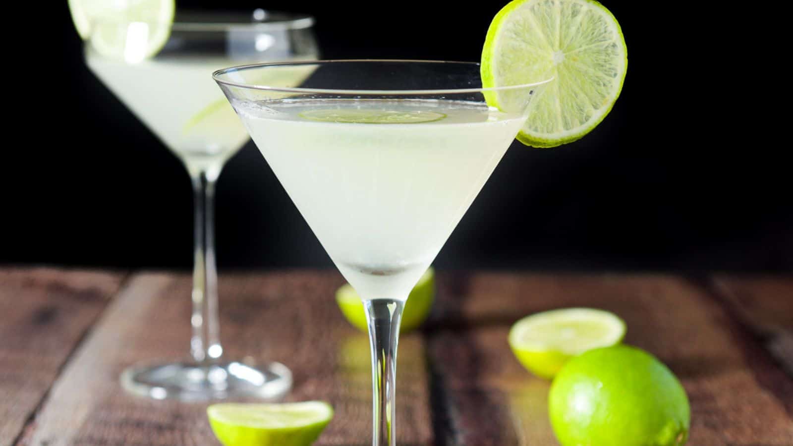 Two martini glasses filled with the lime drink with lime wheels on the rim and limes on the table