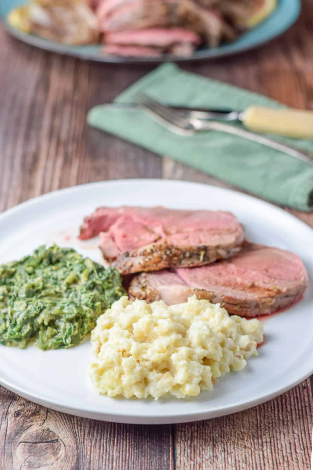 a plate with celery root, spinach, and lamb with more lamb on a platter in the back