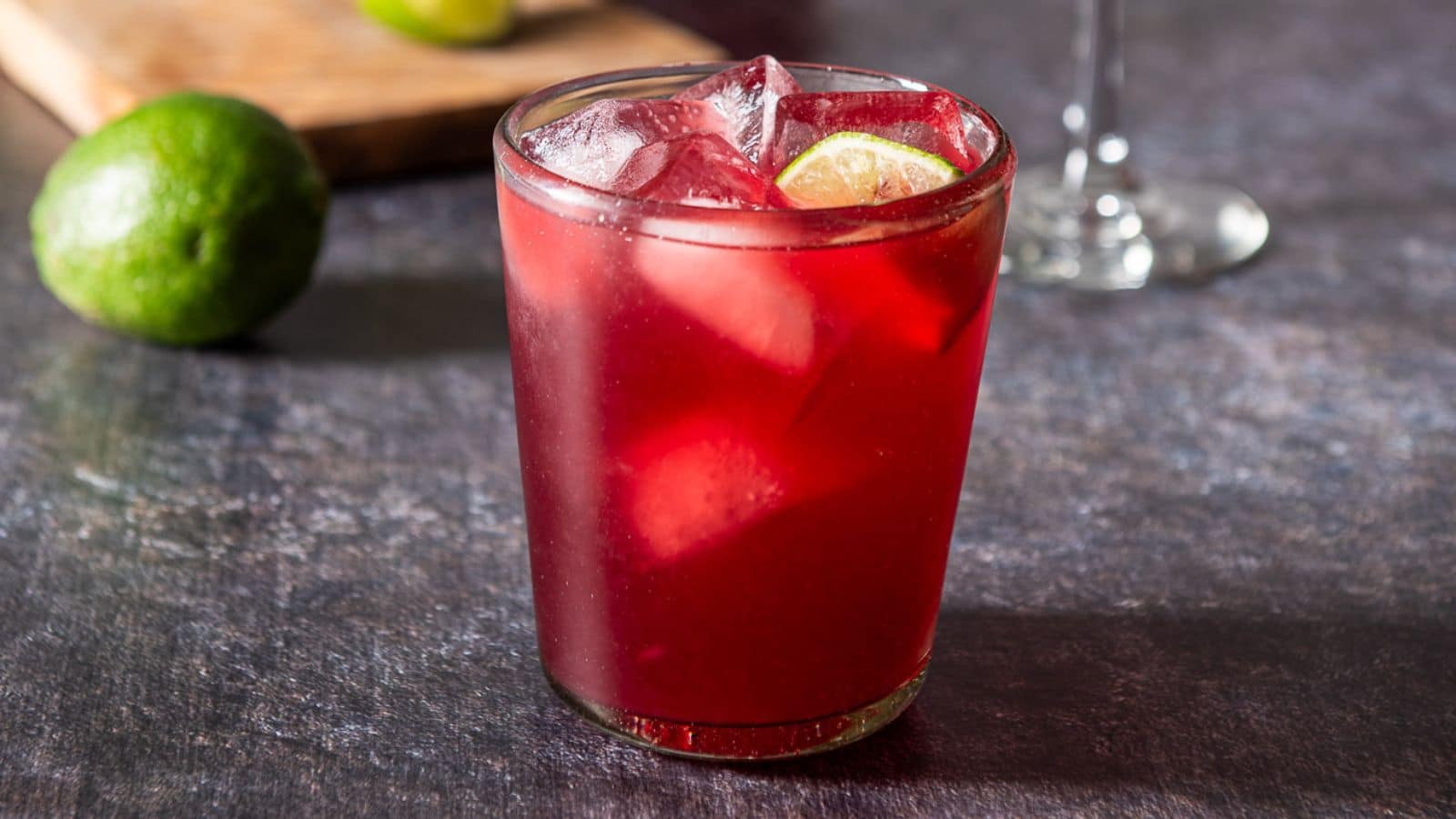 A glass filled with the red margarita with lime in the drink and on the table