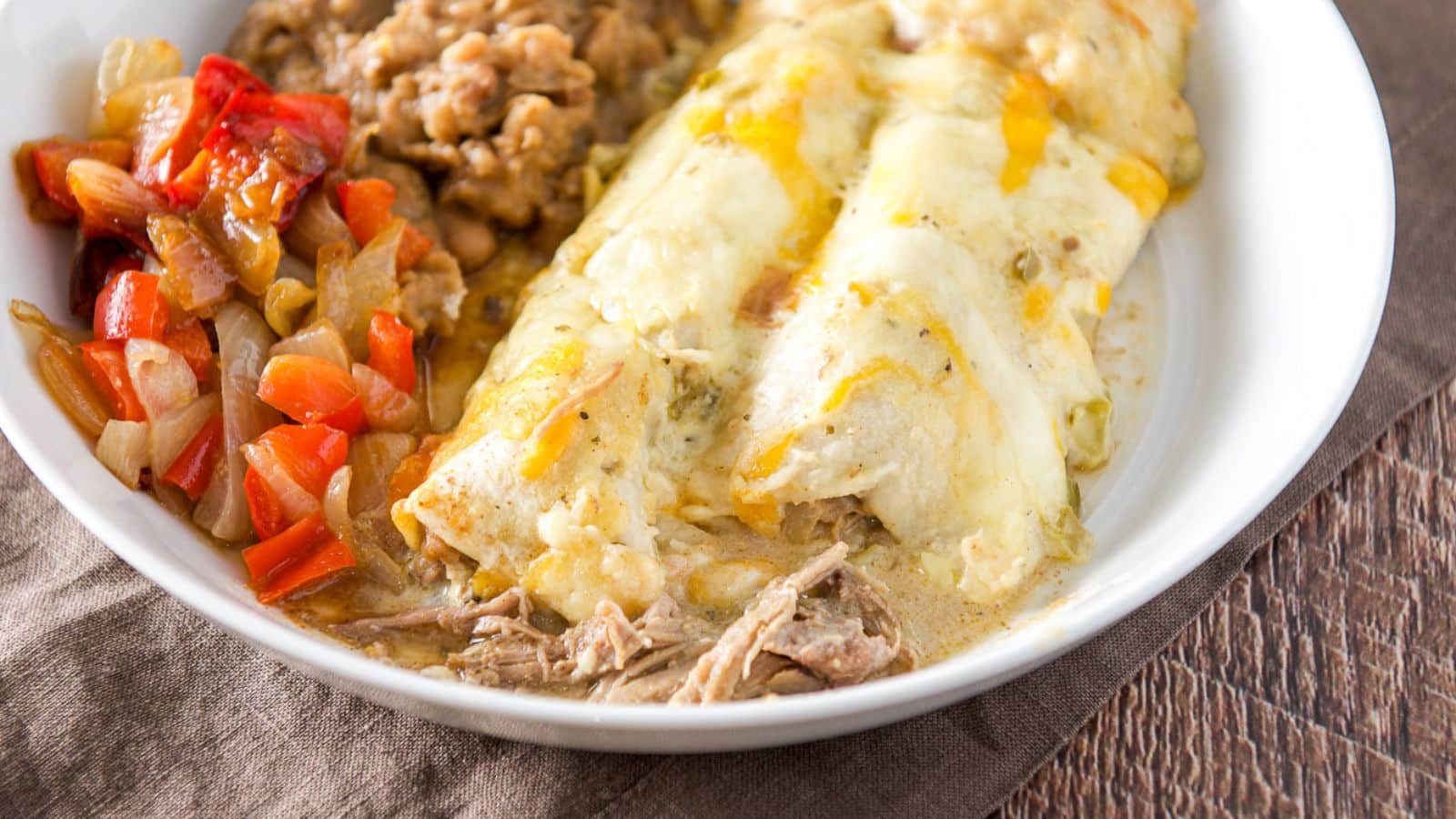 A white deep plate with two enchiladas with veggie and beans