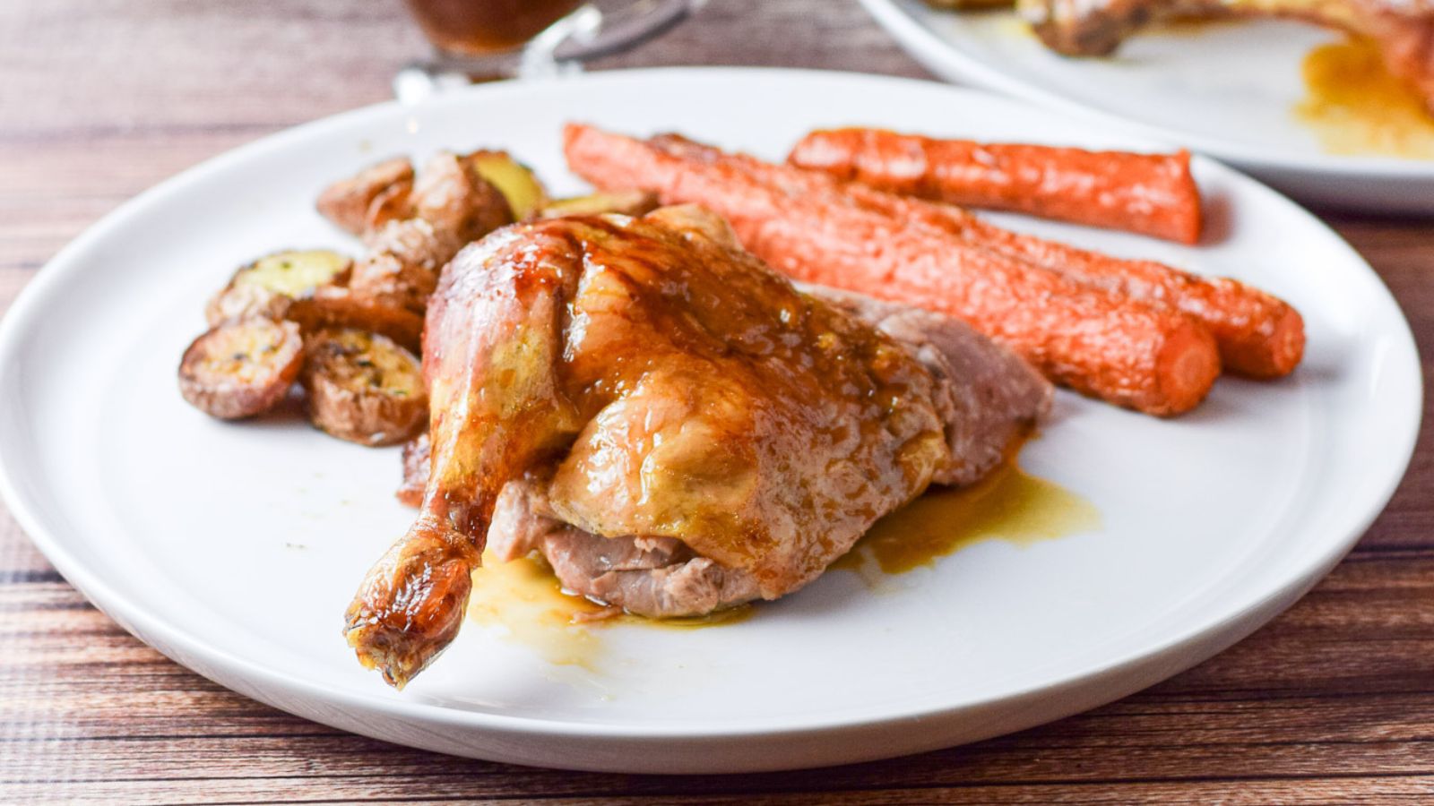 A white plate with a duck leg and thigh along with carrots and potatoes