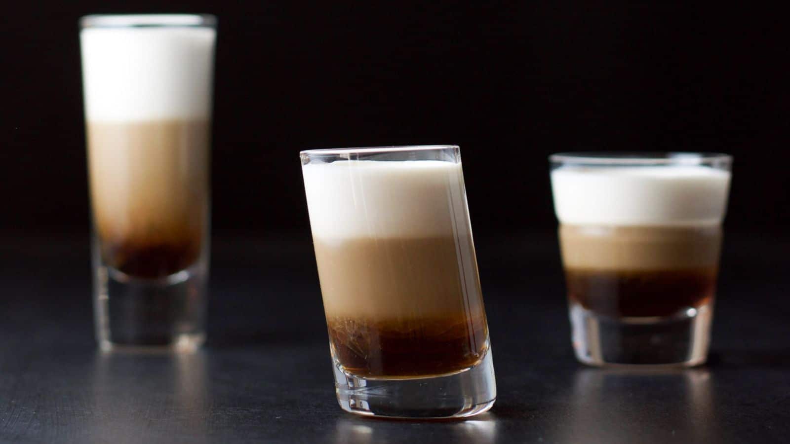 a tilted glass in front of two other glasses with the layers of brown, beige, and cream