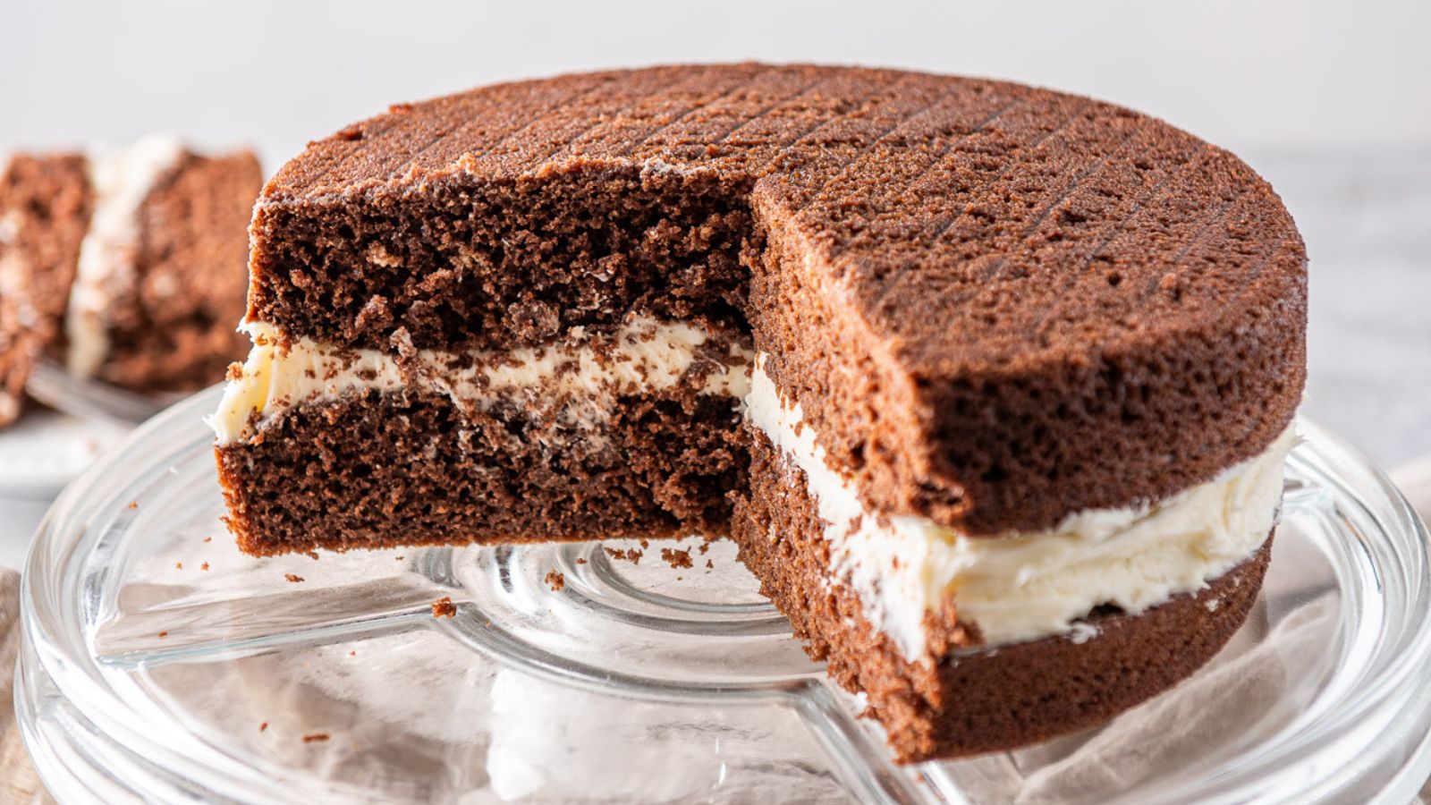 a chocolate cakewith a big piece cut out on a stand with a piece of cake in the back