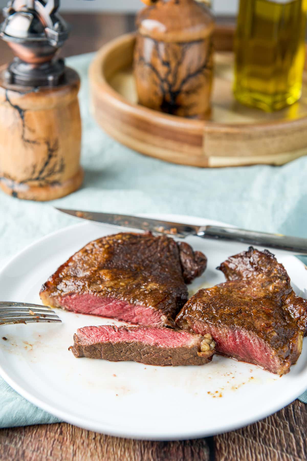 The steak with a piece taken out of it and the rest of the meat cut in half, along with condiments in the back