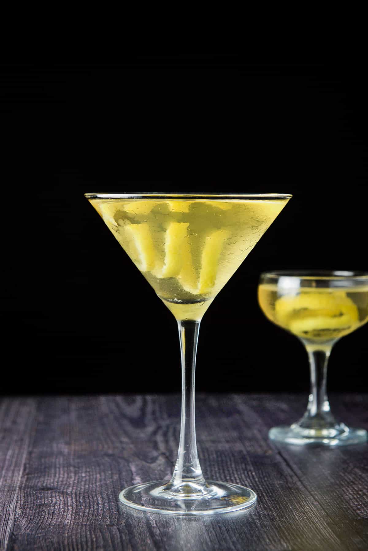 vertical view of the two martini glasses filled with the clear cocktail with lemon twists
