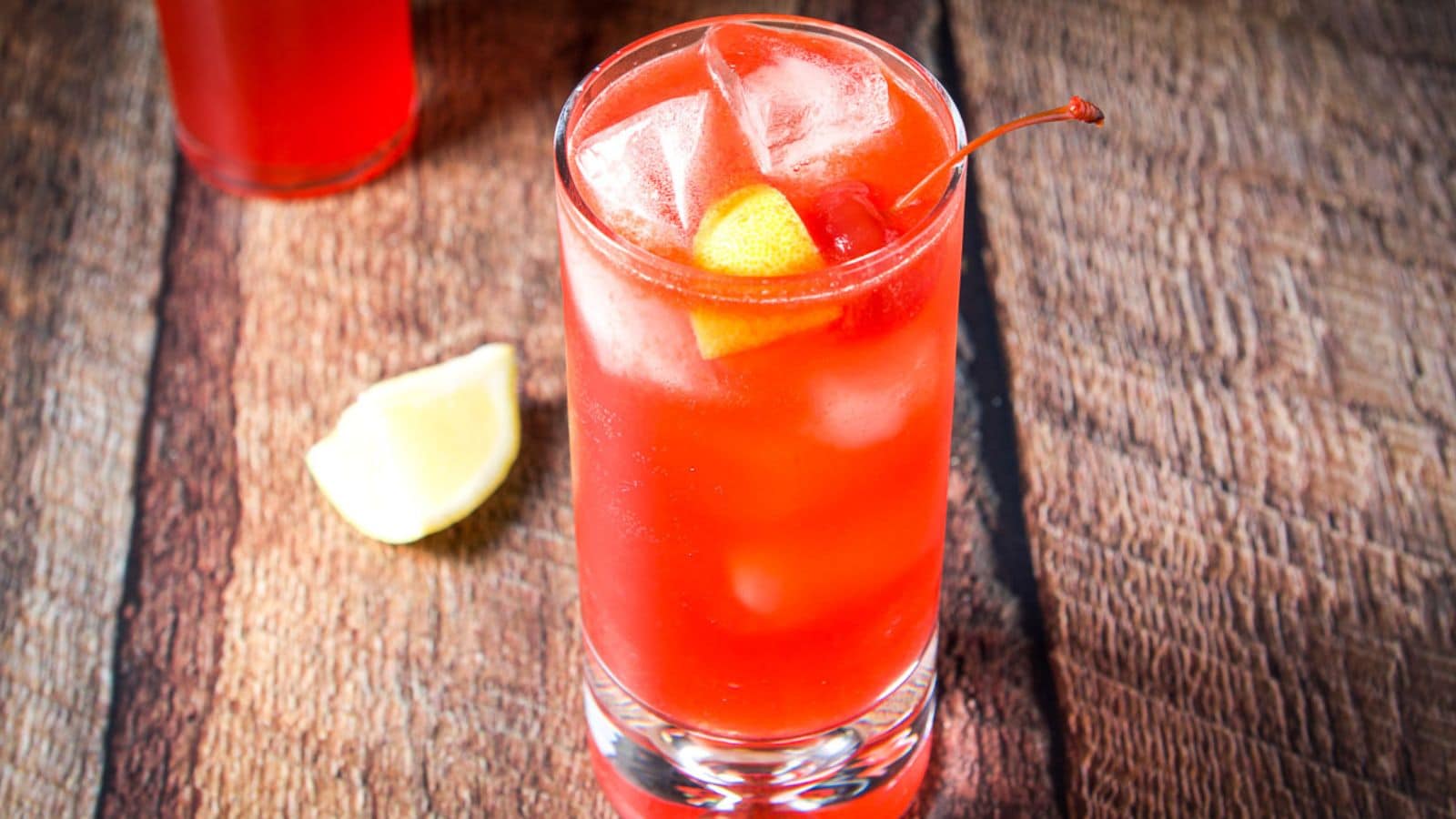 A tall glass filled with the red cocktail with wedges of lemon