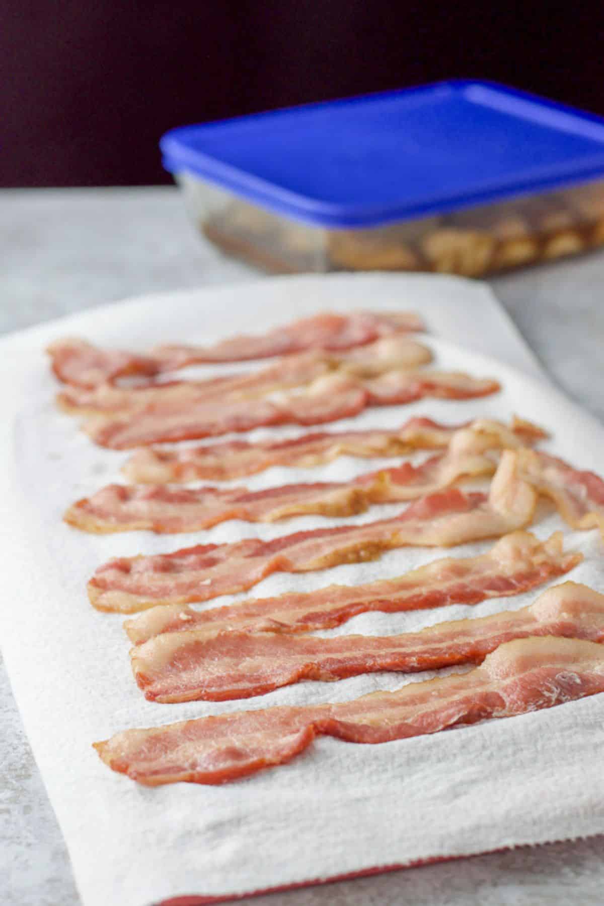 Bacon partially cooked and laying on a paper towel with the scallops in the background marinating