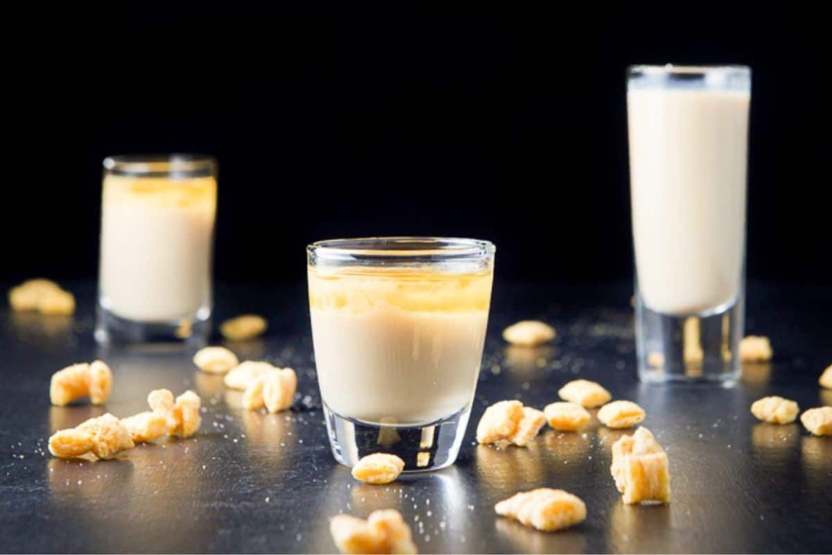 Three different sized shot glasses filled with the layered cream shot with captain crunch on the table