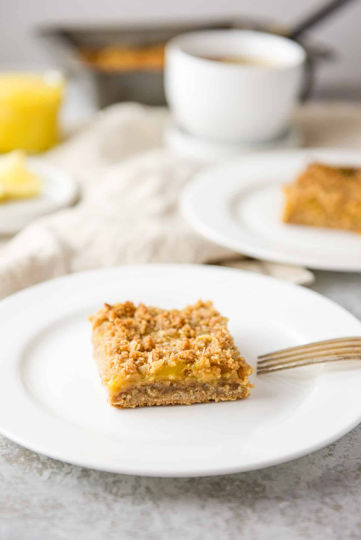 Closer view of the lemon bars on two plates with tea, lemon and the pan behind them
