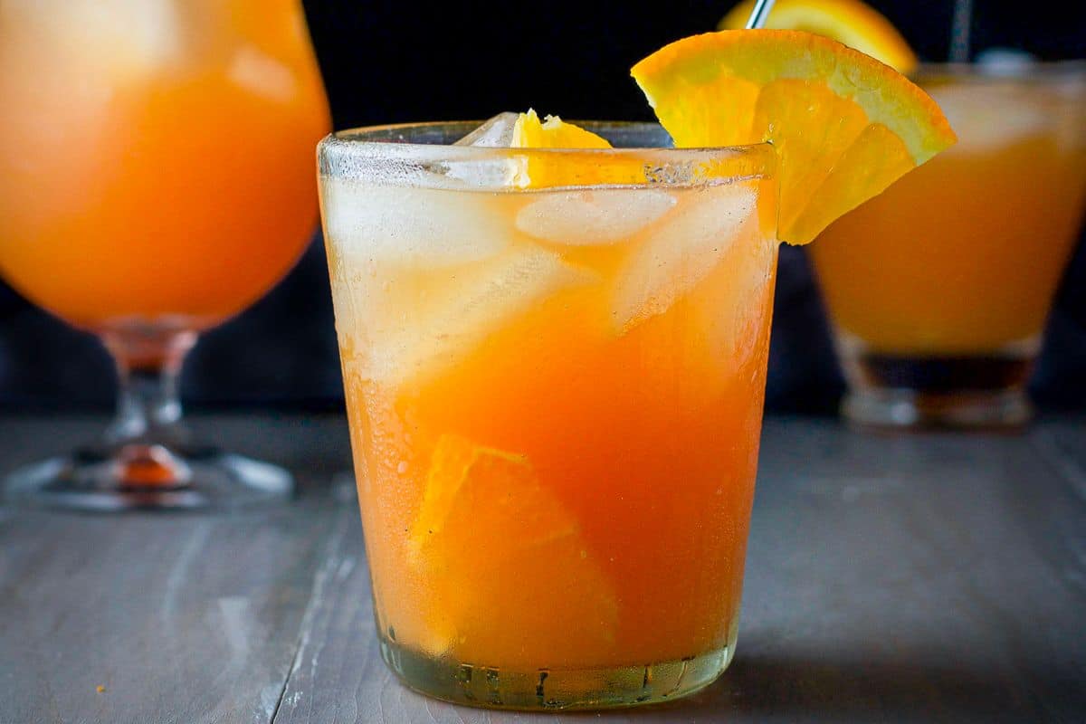 Double old fashioned glass filled with the swizzle with a stirrer in it with two glasses in the back