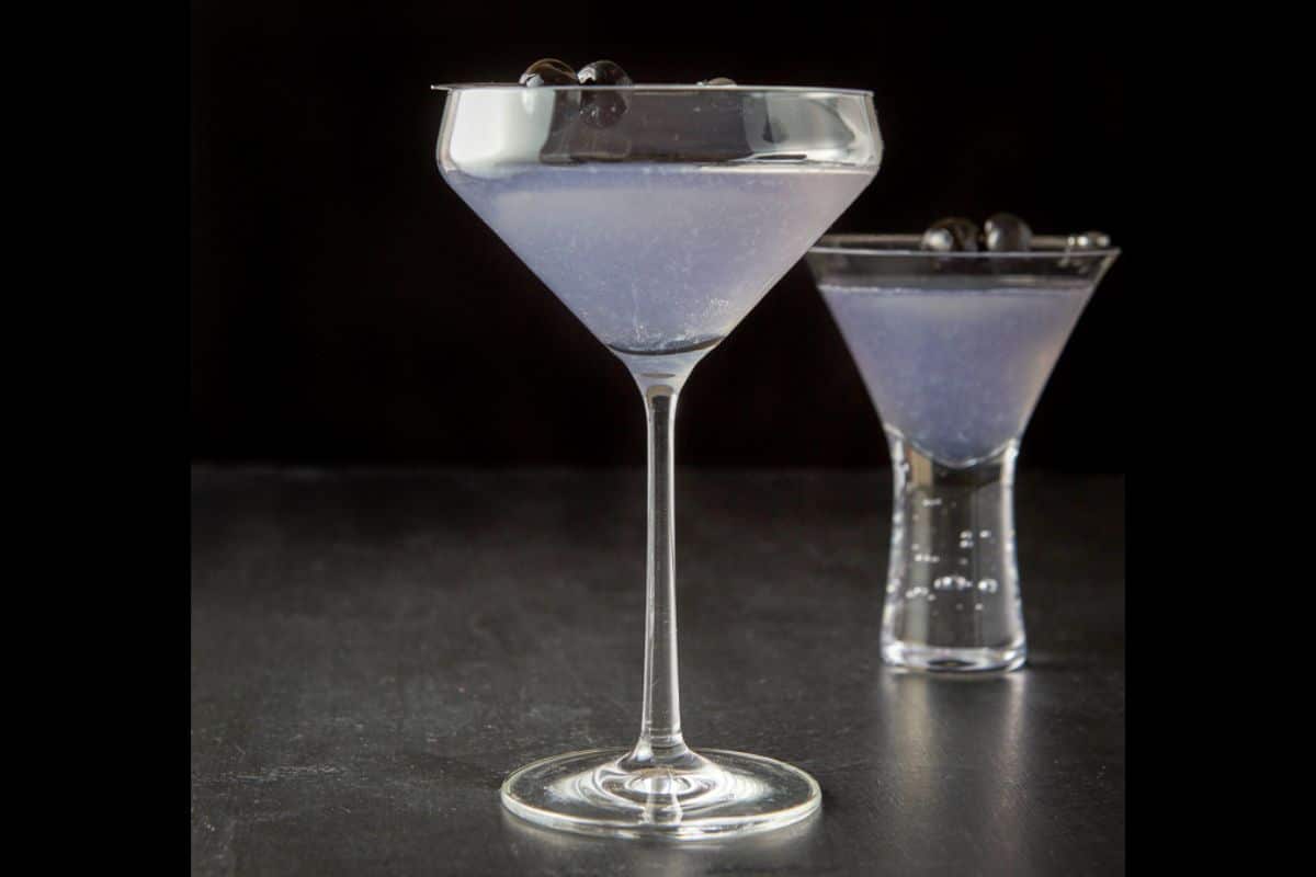 Vertical view of the curved martini glass with cherries as garnish. There is a bubble glass in the background