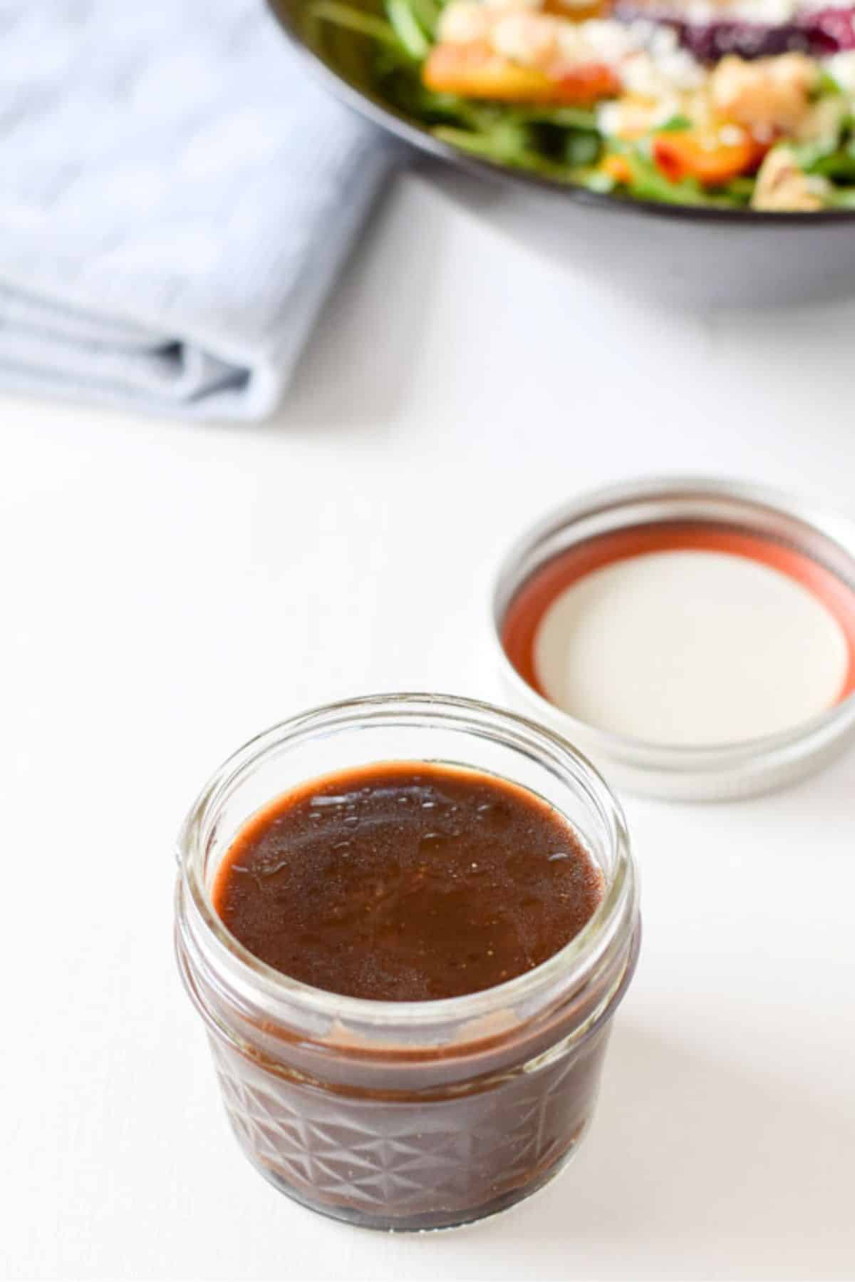 A small jar filled with the vinaigrette with a salad in the background