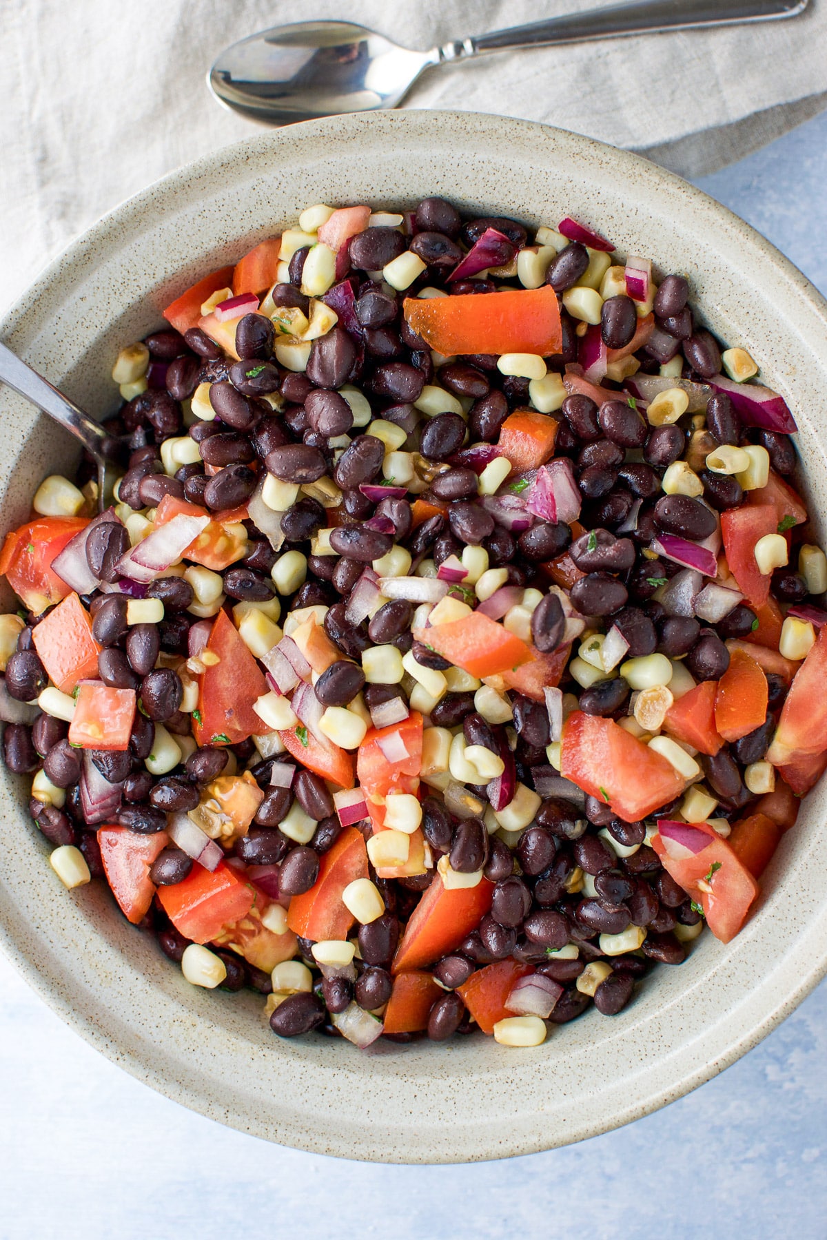 Overhead shot of a beige bowl with the bean salad and a few spoons and napkin in the background