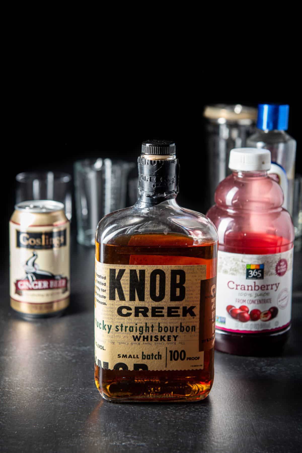Bourbon, cranberry, ginger beer, and simple syrup on a board with glassware