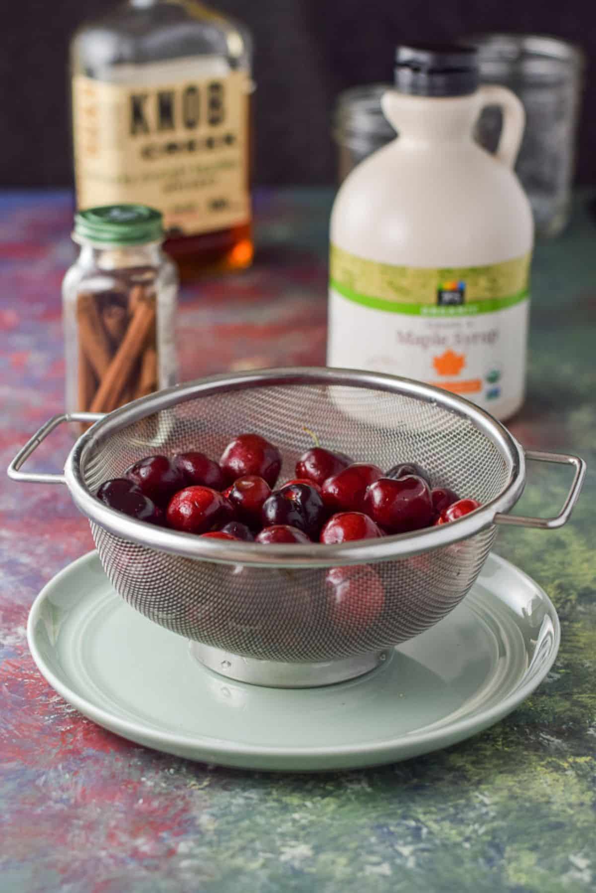 Cherries, cinnamon sticks, bourbon and maple syrup for the bourbon soaked cherries Cherries, cinnamon sticks, bourbon and maple syrup on a colorful table